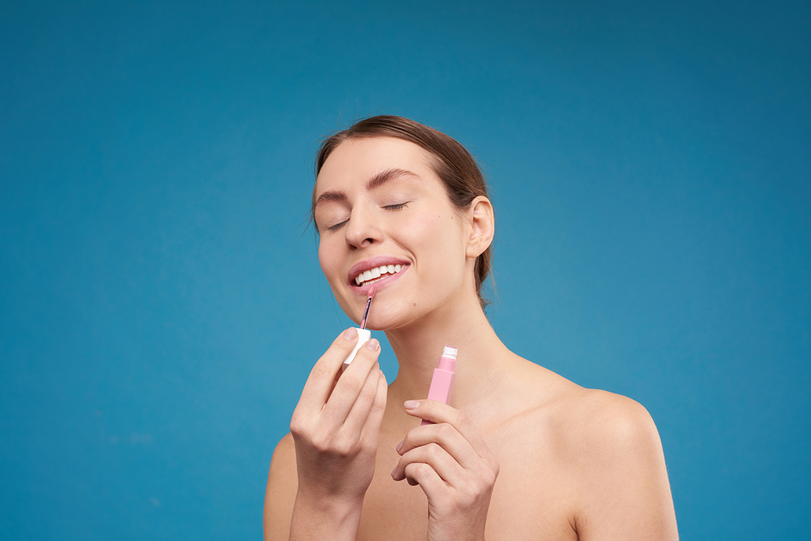 A woman applies a pink lip gloss made from natural raw materials to her lips